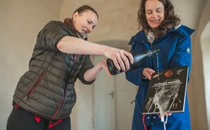 Tereza Sýkora Řeháková křtí knihu Ústřice a breviář, již přidržuje Marcela Waldmannová, vedoucí výzkumu jímky a iniciátorka tohoto publikačního počinu, nad samotnou jímkou. Foto T. Chlup, 2024.